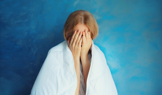 Upset sad crying woman covering her eyes with her hands with blanket while experiencing mental suffering at home