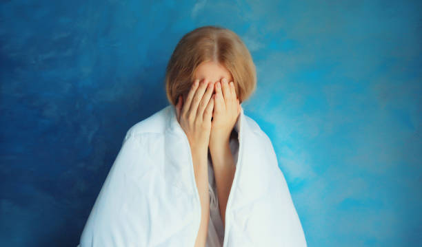 Upset sad crying woman covering her eyes with her hands with blanket while experiencing mental suffering at home stock photo