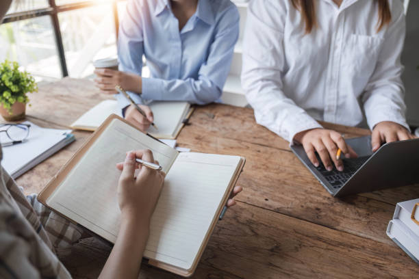 istock Asian College groups of students using laptop, tablet, studying together with notebooks documents paper for report near windows in classroom. Happy young study for school assignment, Soft focus 1694877074