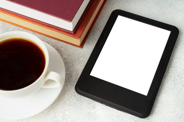 istock Composition with modern e-book reader, hardcover book and cup of coffee on table 1694884725