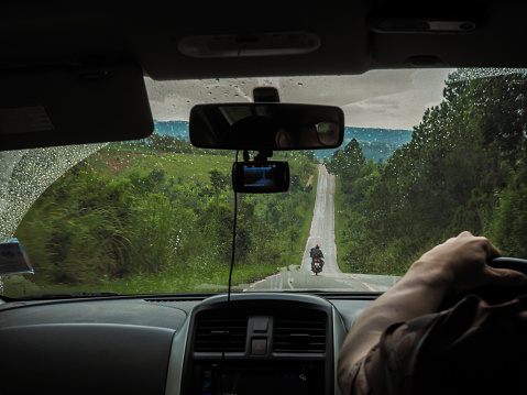 Driver Point of view. Driver driving off road drive car on the mountain green forest country road in rainy day. inside car windshield view point. Safely auto driving concept. Scenery. The paved road with a slope on the hill. surrounded by green forest sunny outdoors.