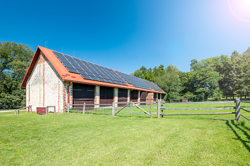 Big brick barn on a farm. Solar panels installed on the roof of the barn.