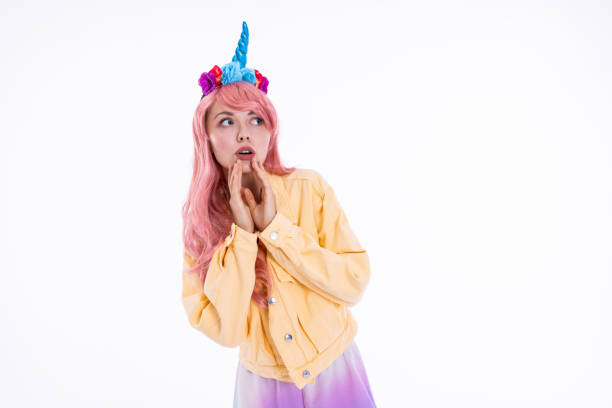 istock Young model showing different emotions looking into distance thoughtfully in unicorn headband and pink wig wearing yellow denim jacket posing while shooting process 1694930251