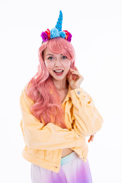 istock Happy smiled model girl on white background in studio looking at camera smiling in good mood wearing pink wig and unicorn headband posing for fashionable magazine in yellow denim jacket 1694930435