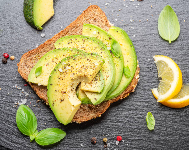 istock Avocado toast - bread with avocado slices on natural slate serving board. Top view. 1694935917