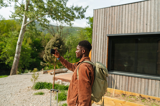 Photo of a young African American man, who has jus arrived into his rental home for the weekend - a cabin on the riverbank in the woods; He is capturing photos on his smart phone of the beautiful nature that surrounds him