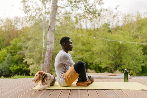 Photo of a young African American man practicing yoga poses early in the morning, right after he starts his day. He is working out outdoors on the front porch of his house.