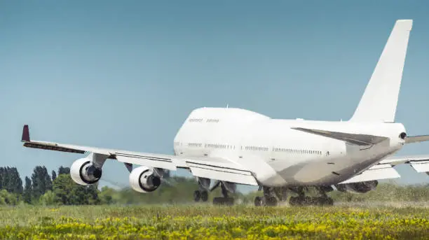 hot exhaust coming out of the engine and distorts the visibility. Rear three quarter view of jumbo jet lifts off blowing off dust and plant seeds