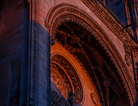 Detail of the ornaments of the new cathedral of Salamanca with bas-reliefs of religious motifs, from a low angle view, illuminated by the golden and orange light of sunset with projected shadows.