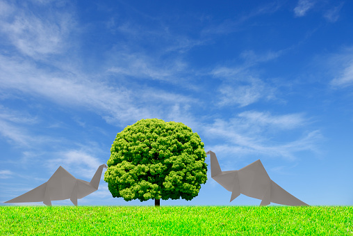 Two Origami herbivore dinosaur foraging and camphor tree against blue sky with copy space.