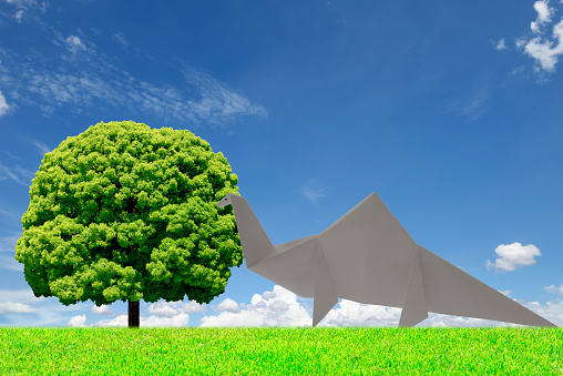 Origami herbivore dinosaur foraging and camphor tree against blue sky with copy space.