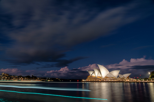 Sydney, Australia - July 23, 2023: Evening descends upon Sydney, and the iconic form of the city's Opera House can be seen across the waters of Circular Quay. Long exposure photo, capturing light trail left by a passing ferry.