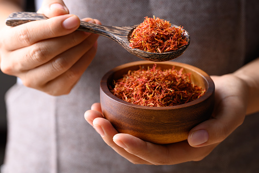 Dried safflower in wooden bowl and spoon holding by hand, Herbal tea
