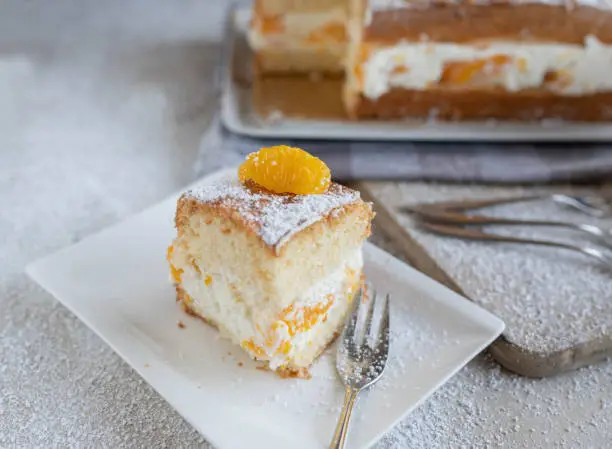 Delicious homemade tangerine cream cake or orange mandarin cake torte. German cuisine. Served sliced on a white plate with fork. Closeup