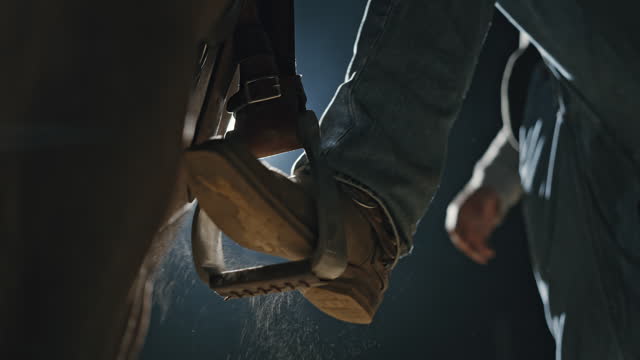 SLO MO Close-Up Shot Of Cowboy Placing Booted Foot into Stirrup and Mounting Horse at Night