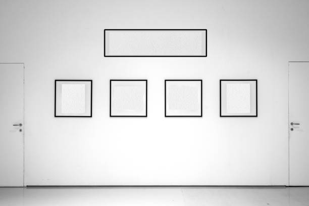 In the white-walled exhibition room, frames with empty interiors are displayed. The white interior of the frames allows the insertion of images or text. Frames aligned between two doors.