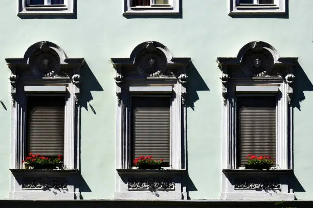 stucco trimmed old decorative wood windows in frontal view. red geraniums in flower pots on the window sills. residential architecture and nature concept.