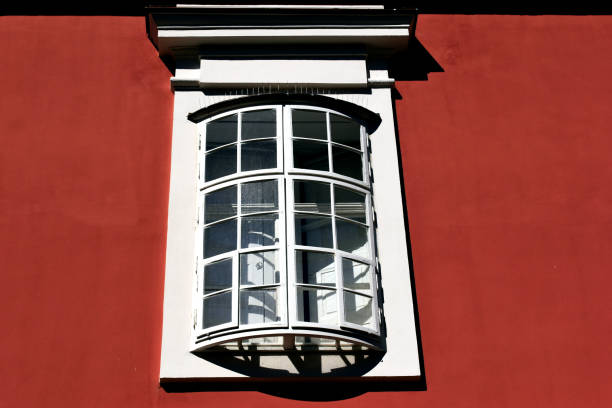 closeup view of old style wood bow window in stucco exterior wall. arched shape with outer operable wings on hinges. strong light. European architecture. textured stucco wall. decorative residential facade