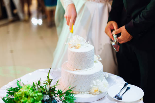istock multilevel wedding cake on a round table. Newlyweds are standing next to one and cutting a wedding cake 1695119012