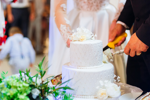 A close-up of a beautifully decorated wedding cake. Newlyweds cut a cake to cater to guests at the wedding