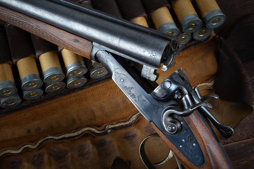 Antique 12-gauge break-action smooth-bored shotgun with paper cases on wooden table.