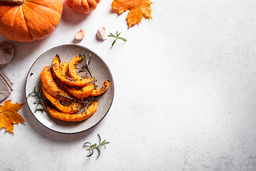 Roasted pumpkin slices with garlic and herbs on white, top view, copy space. Oven baked pumpkin, seasonal autumn side dish or vegan meal.