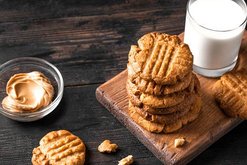 Peanut Butter Cookies and glass of milk on dark wooden table, copy space. Traditional american cookies and peanut spread.