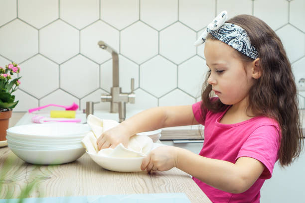 bambina sconvolta che pulisce ciotole trasparenti con asciugamano asciutto sul set da cucina. ritratto di bambino che lava i piatti nel lavello della cucina. - domestic kitchen towel dish cloth rag foto e immagini stock