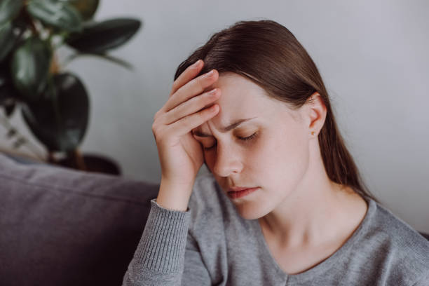istock Tired lady unwell stressed headache suffer depression sitting on couch at home. Upset young woman head pain ache discomfort migraine overworked exhausted frustrated loneliness anxiety worried problem 1695178221