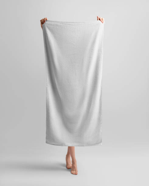 A mockup of a white bath towel, a girl holds it in her hands, in full height, her legs are visible. A mockup of a white bath towel, a girl holds it in her hands, in full height, her legs are visible. Template of textured soft towelette isolated on background. Personal hygiene product for dry body. woman wrapped in bath towel stock pictures, royalty-free photos & images