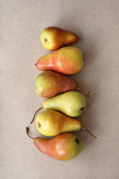 Red and yellow pears stack in a row on neutral beige background, flat lay.