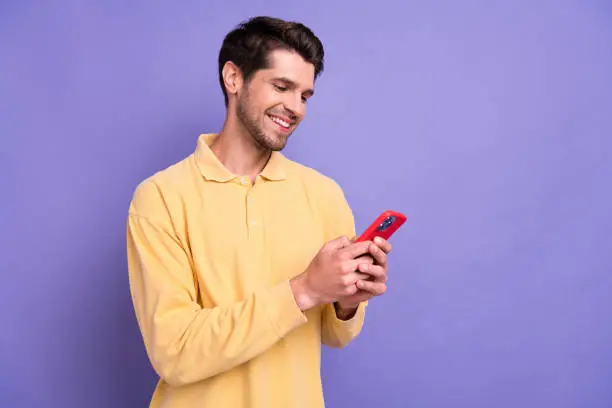 Photo of sweet good mood man dressed yellow shirt chatting modern device empty space isolated purple color background.
