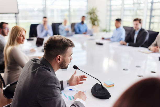 istock Young businessman talking on a microphone during a meeting at conference table. 1695204070