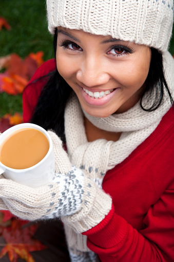 Happy Filipino female sitting on Autumn leaves having a fresh homemade cup of coffee