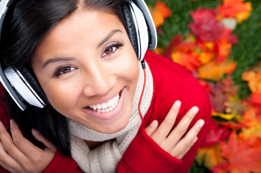 Smiling filipino woman listening to music sitting on Autumn fallen leaves