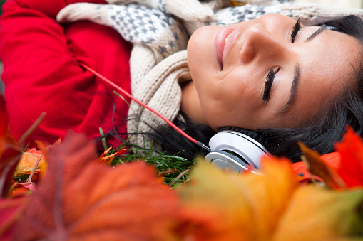 Smiling filipino female listening to music laying on Autumn fallen leaves
