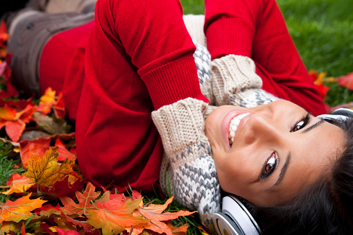 Smiling filipino woman listening  to music laying on Autumn fallen leaves