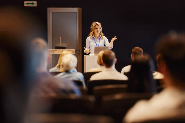 Happy female speaker giving a speech in front of people at convention center. Copy space.