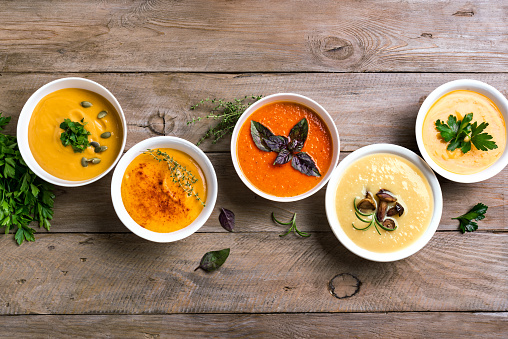 Autumn soups. Set of various seasonal vegetable soups and organic ingredients on wooden background, top view, copy space. Homemade colourful seasonal vegan soups.