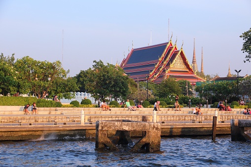 People visit Chao Phraya riverbank with Wat Pho temple in background in Bangkok. Bangkok is the biggest city in Thailand with 14 million people living in its urban area.