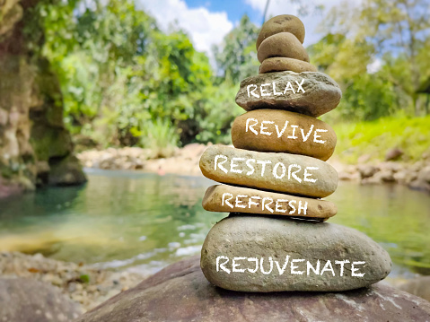 Relax, revive, restore, refresh and rejuvenate text written on pebbles stack with nature background  Wellness lifestyle concept.
