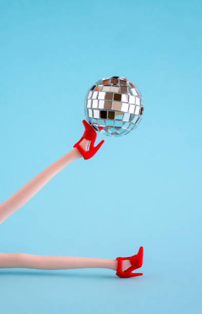 istock Doll legs in red shoes with disco ball on blue background. 1695262402