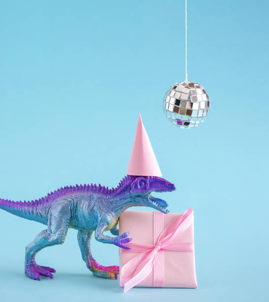istock Cute blue and violet dinosaur wearing party hat and holding present box on blue background. 1695262465
