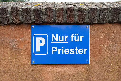blue and white sign Parking for Priests only on a stone wall