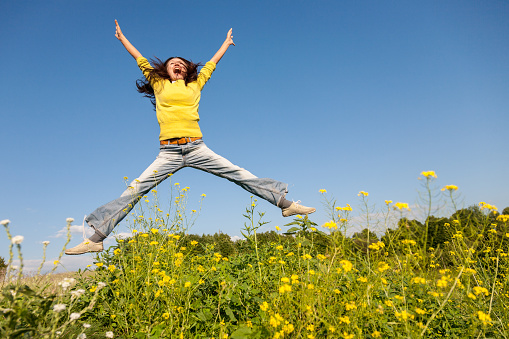 Happy and beautiful young woman in a bright yellow sweater and blue jeans  jumping high in a sunny summer field. Happiness and joy lifestyle concept