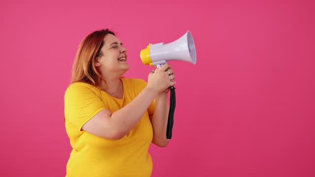 Young Woman Talking Into The Megaphone Against A Pink Background