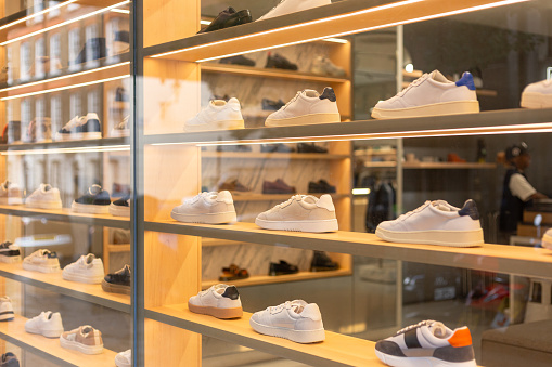 Retail display of trendy sneakers displayed in the window of a shoe shop in central London, UK. The sneakers are displayed neatly in a row. The interior of the shop is defocused in the background. Room for copy space.