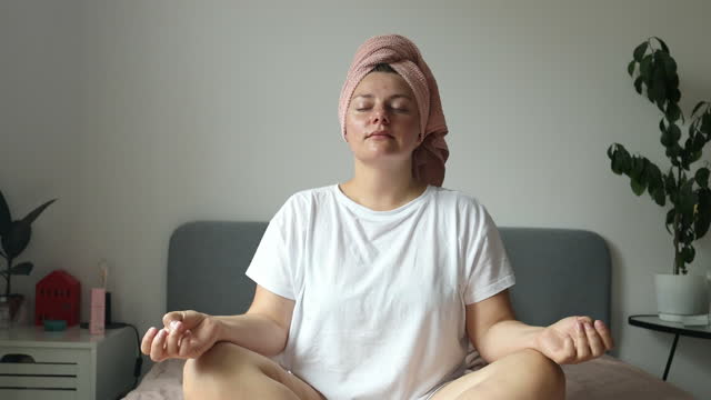 Caucasian girl in casual wear are meditating sitting on bed. Young woman doing yoga exercise at home for stress relief relaxing from work. Dolly slider shot
