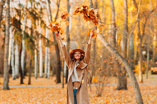 Girl in beautiful autumn park throw up orange leaves. Fall autumn season fashion