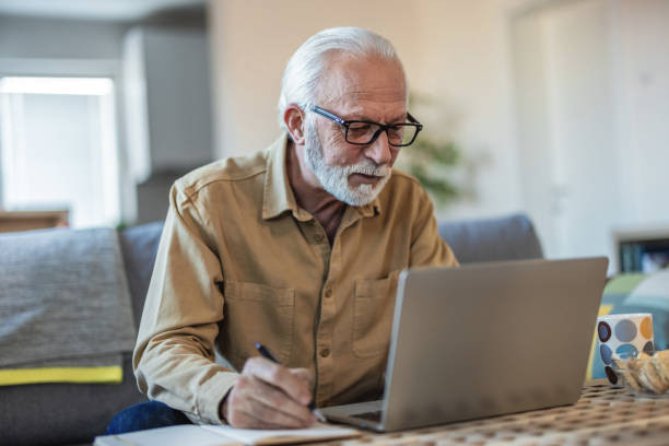 istock Shot of a senior man using a laptop while going over his bills and finances at home. Cropped shot of a senior man going through his finances while sitting at the dining room table. 1695331493